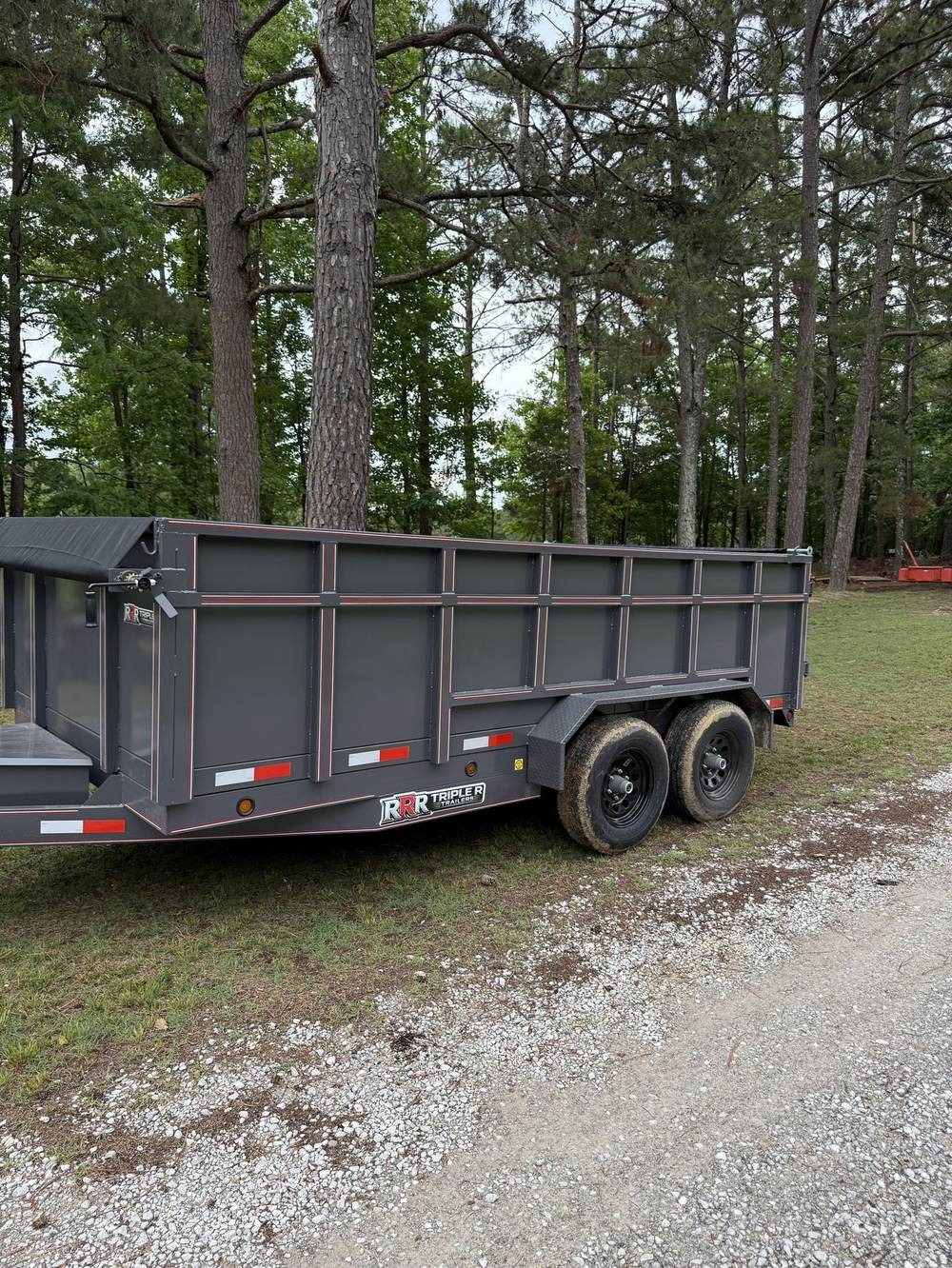Gray Triple R dump trailer with roll tarp on a gravel drive